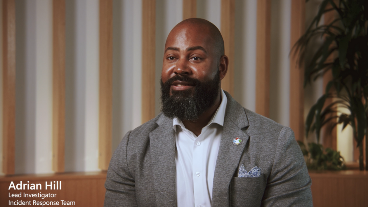 Headshot of man sitting in gray suit in front of a striped backdrop