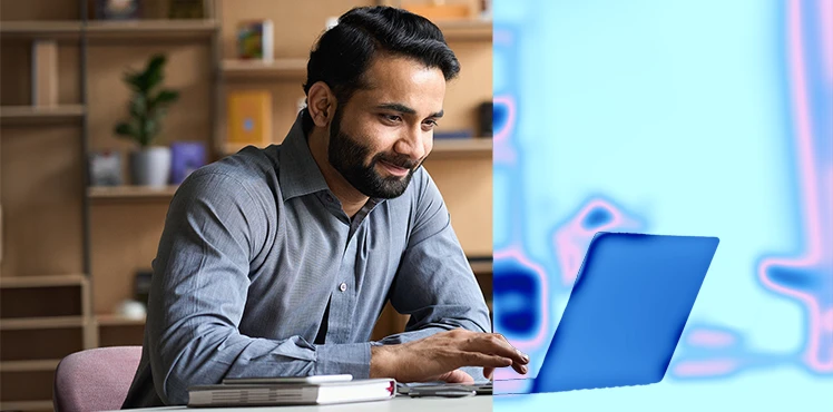 A professional man working on a laptop at his desk in a modern office setting.