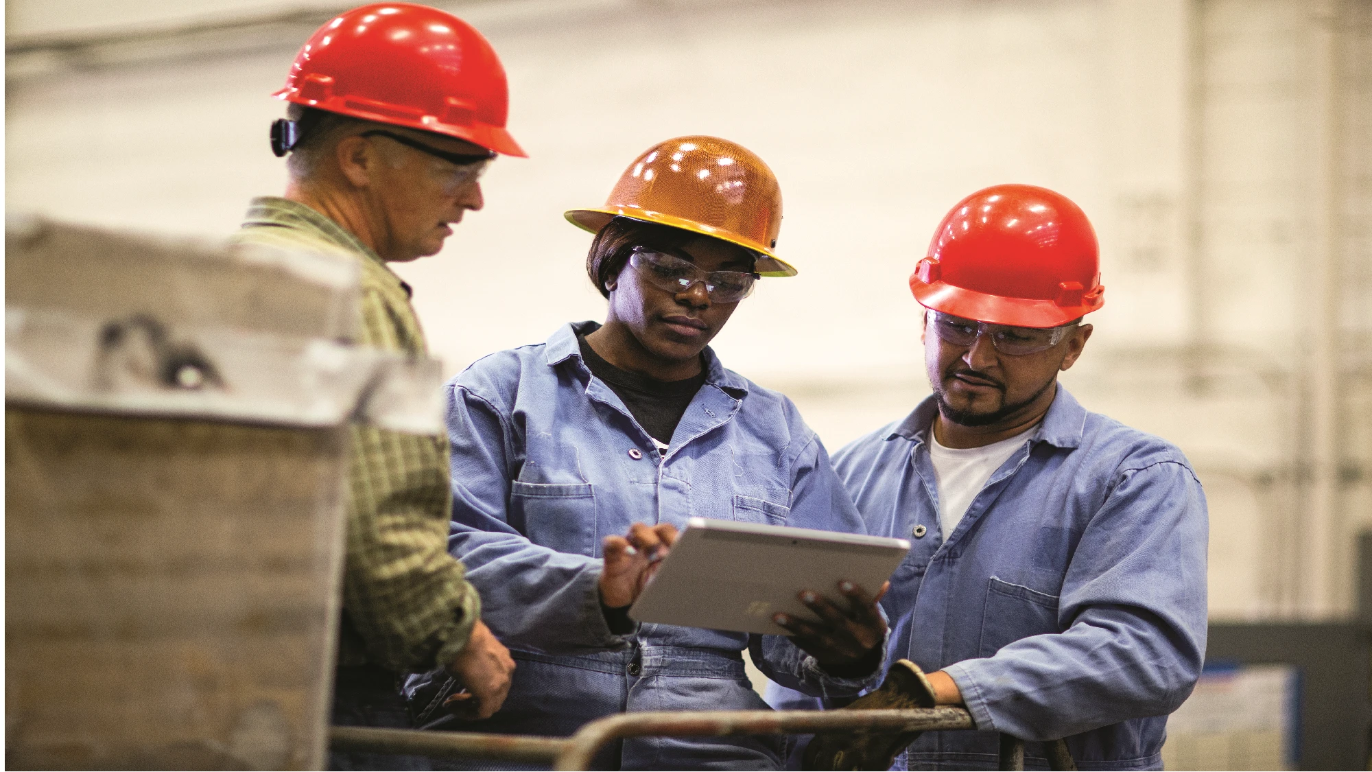 Three workers wearing hard hats look at a Microsoft Surface tablet.