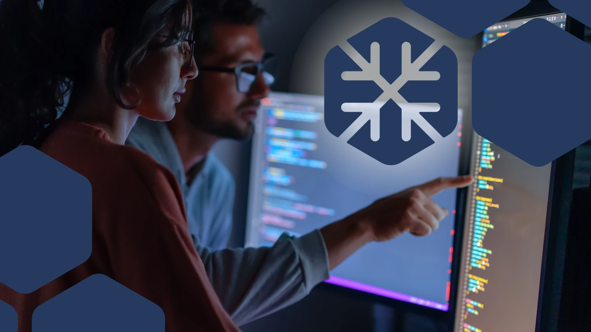 A woman and man reviewing code on various monitors while pointing at the closest screen