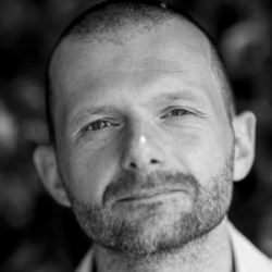 James Rowland-Jones wearing a suit and tie looking at the camera