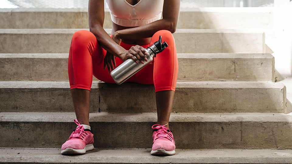 A woman in activewear holding a water bottle rests on a staircase