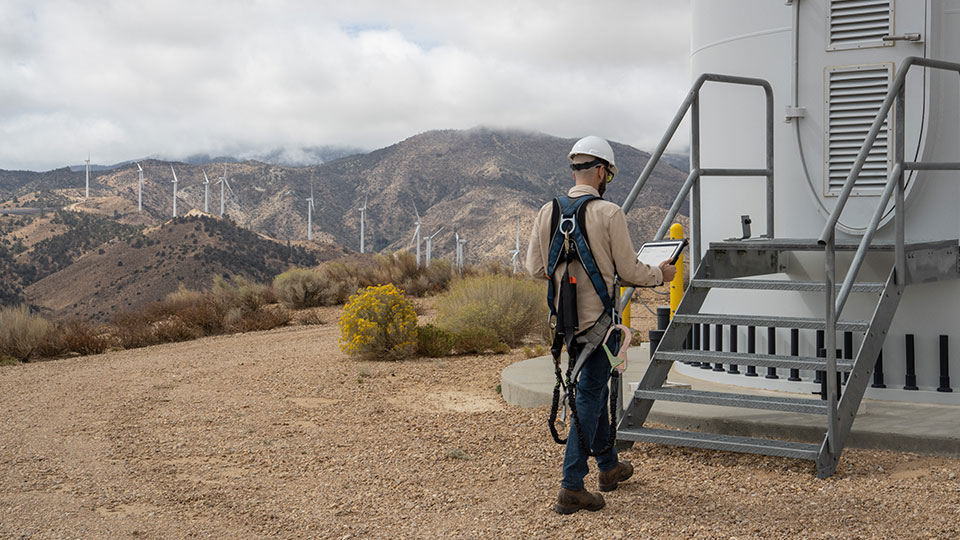 A man in safety gear at a windmill farm consults information on a tablet