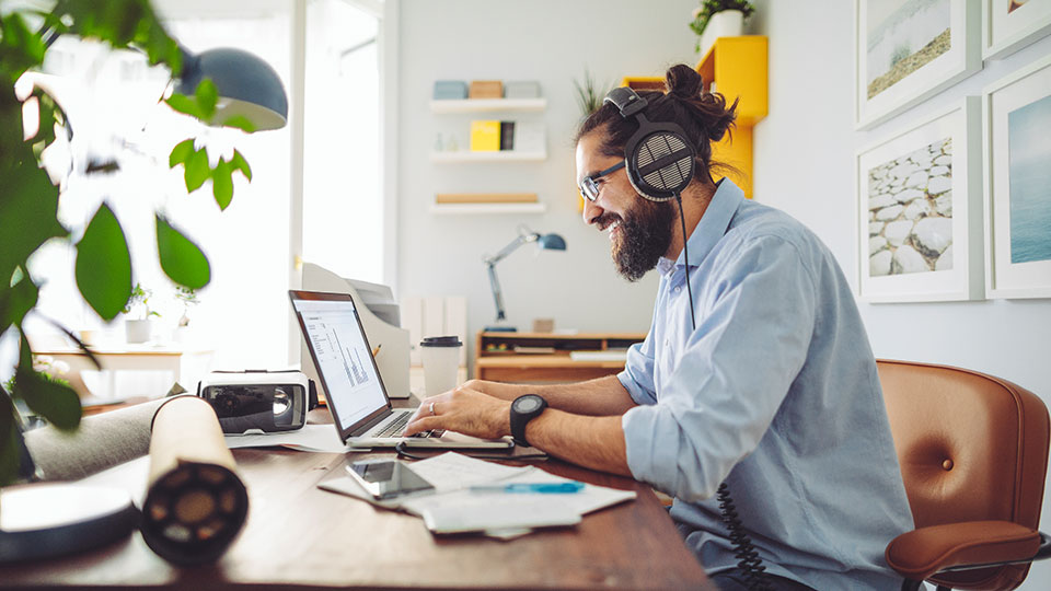 A man wearing headphones smiles while working at his laptop