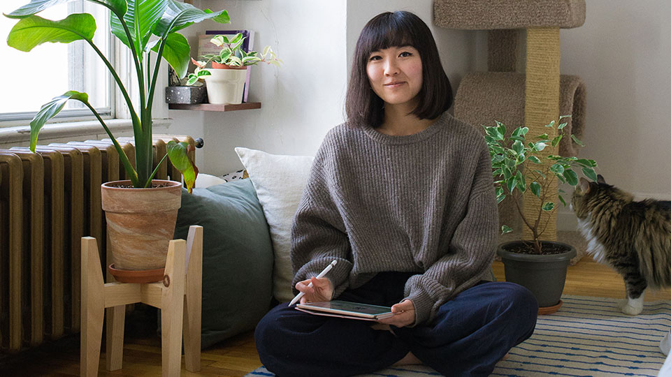A woman in a home environment sits comfortably on the floor with a tablet and stylus