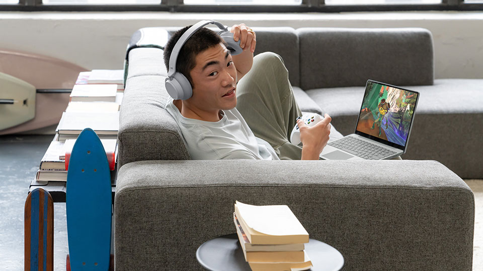 A man on a couch with a game controller slips his headphones off