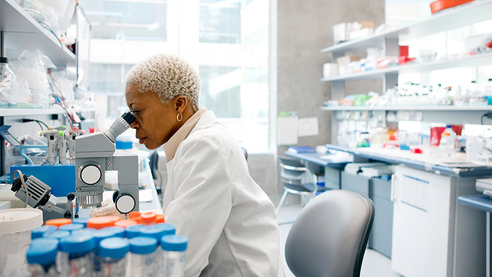 A scientist looks through a microscope in a lab