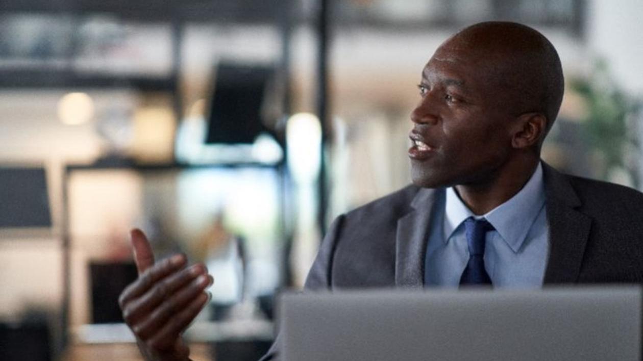 A Chief Technology Officer in a gray suit sits in front of an open silver laptop having a serious discussion.