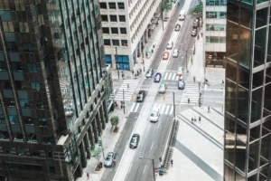 Vue de la rue du centre-ville depuis un angle élevé à l'intérieur d'un immeuble de bureaux. Les voitures traversent l'intersection dans une rue à sens unique. Quelques piétons sont visibles sur les trottoirs et aux passages pour piétons.