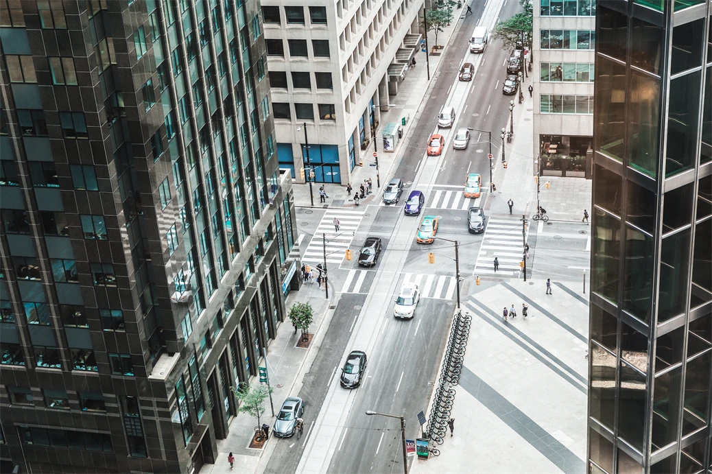 Vue de la rue du centre-ville depuis un angle élevé à lintérieur dun immeuble de bureaux. Les voitures traversent lintersection dans une rue à sens unique. Quelques piétons sont visibles sur les trottoirs et aux passages pour piétons