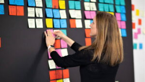 Tricia Fejfar writes on a sticky pad on a whiteboard covered with dozens of sticky pad notes.