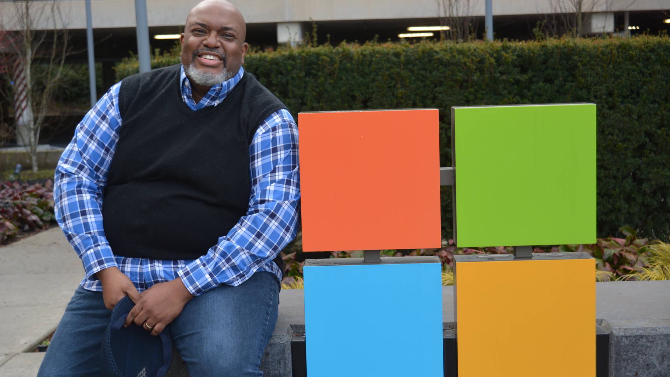 Dwight Jones sits next to the Microsoft sign on the edge of the Microsoft campus. He is smiling.