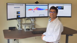 Jayapalan stands in front of his three-monitor workstation in his office.
