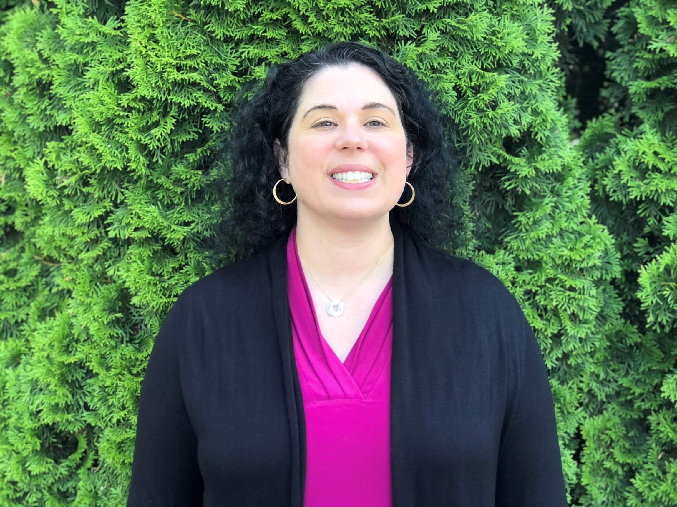 West smiles as she stands outside in front of some plants.