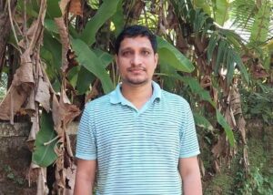 Renjuraj T, wearing a striped polo, stands outside in front of a plant.