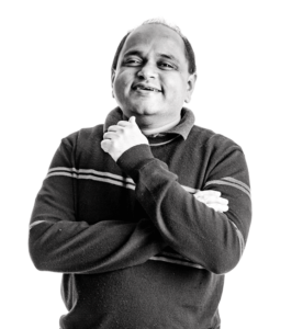  Agrawal smiles as he stands looking at the camera with his arms folded.