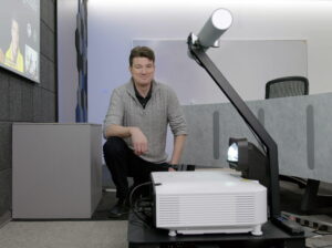 Hempey kneels in behind a projector used to power one of the new meeting experiences being developed in The Hive. 