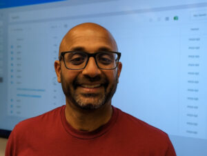 Abraham smiles as he stands in front of a full-size wall screen.