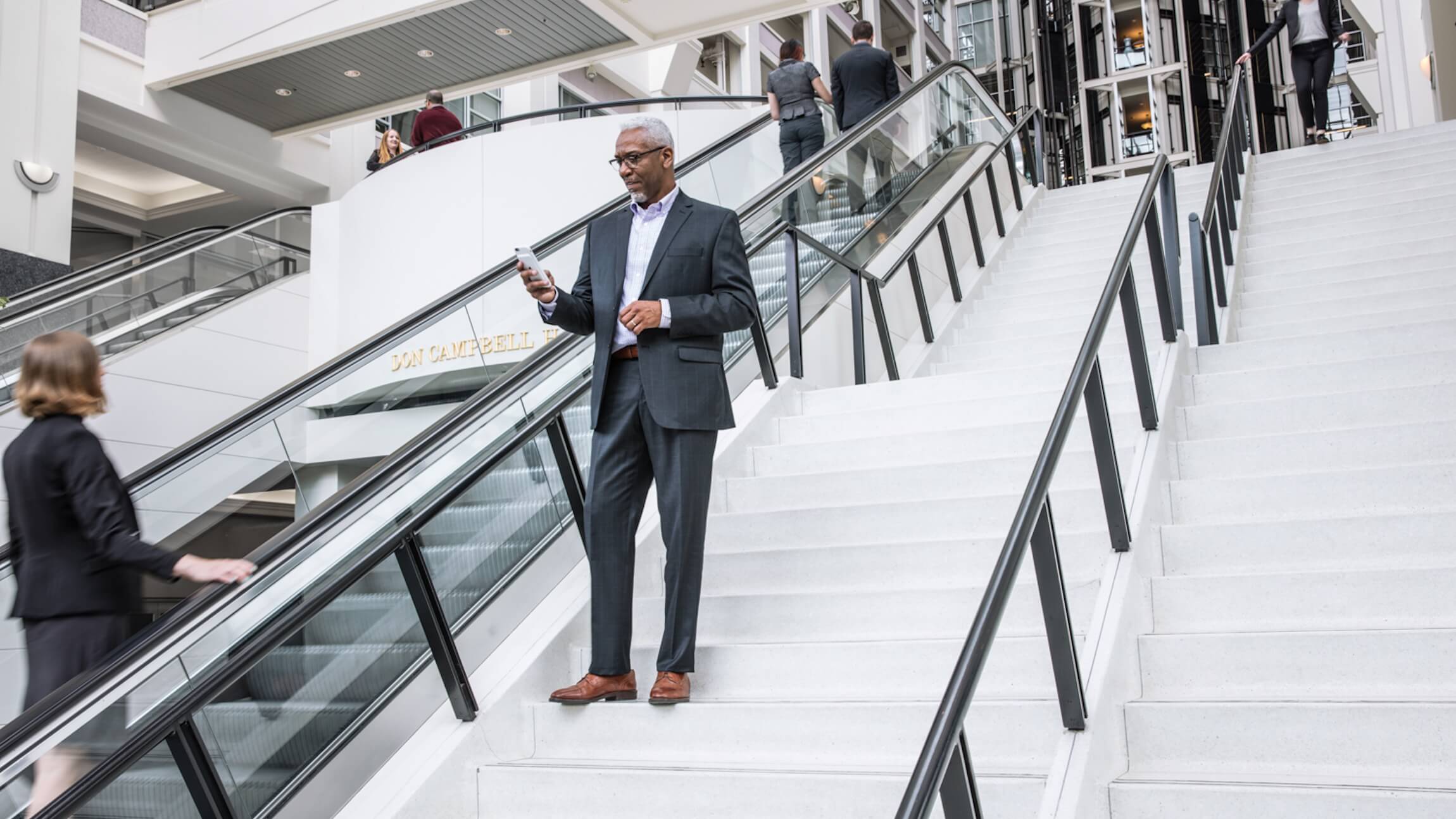 A business executive looks at a mobile phone on an outdoor staircase outside of a large city office building.