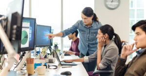 オフィスで同僚社員にモニターを指さしながら何かを伝える女性