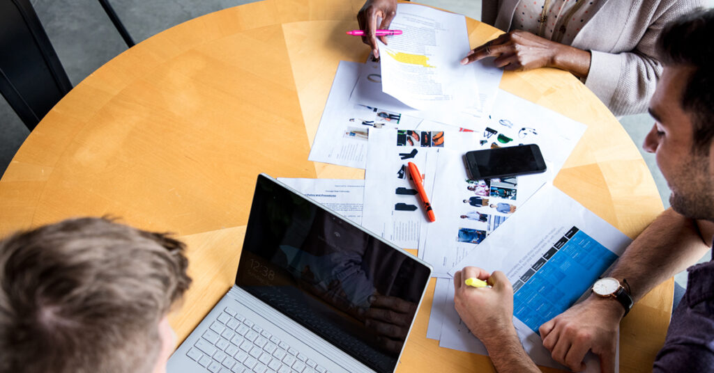 ドキュメントとPCが広げられたデスクでミーティングをしている