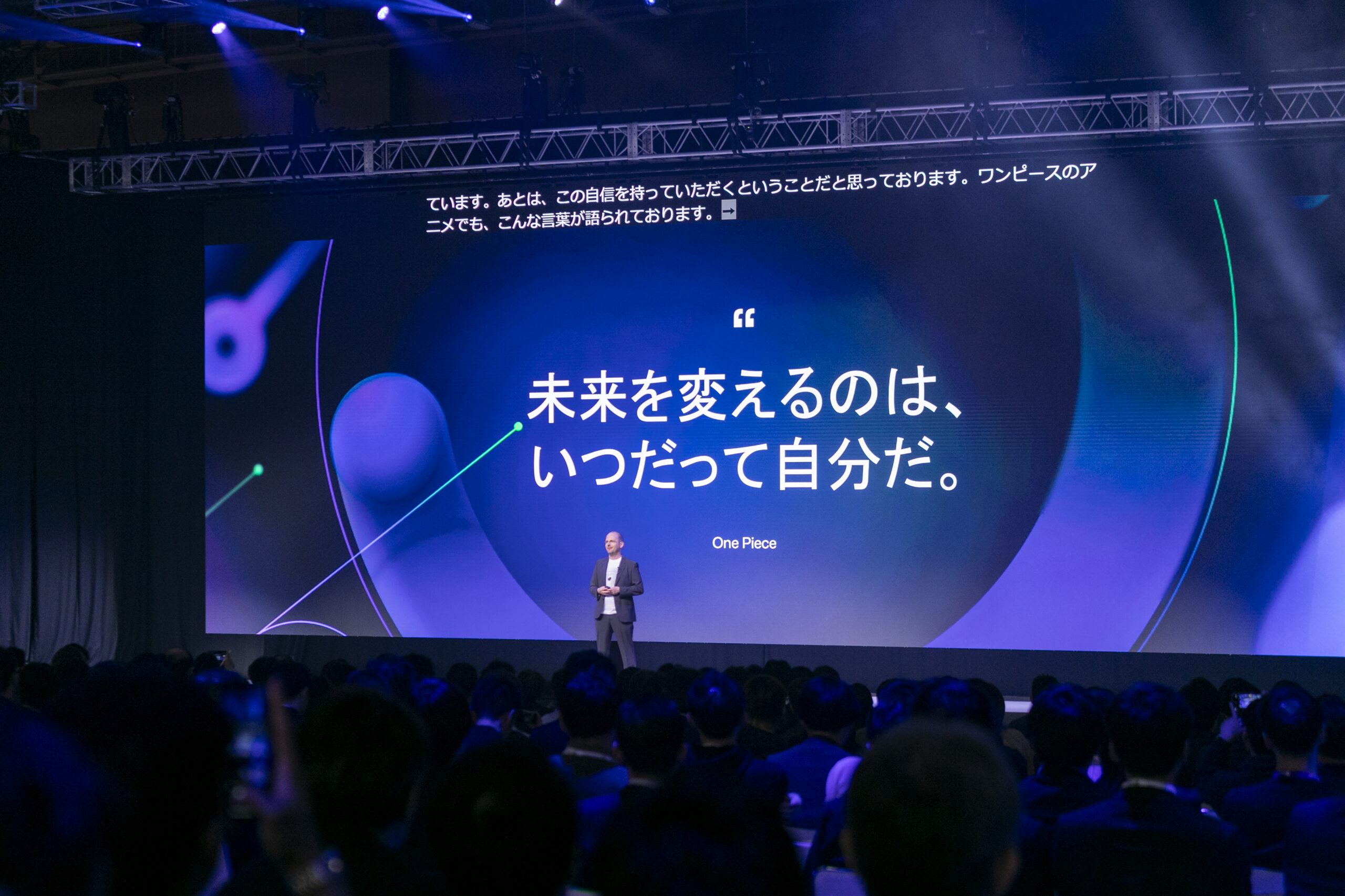 A man standing on a stage with a large screen with a crowd of people