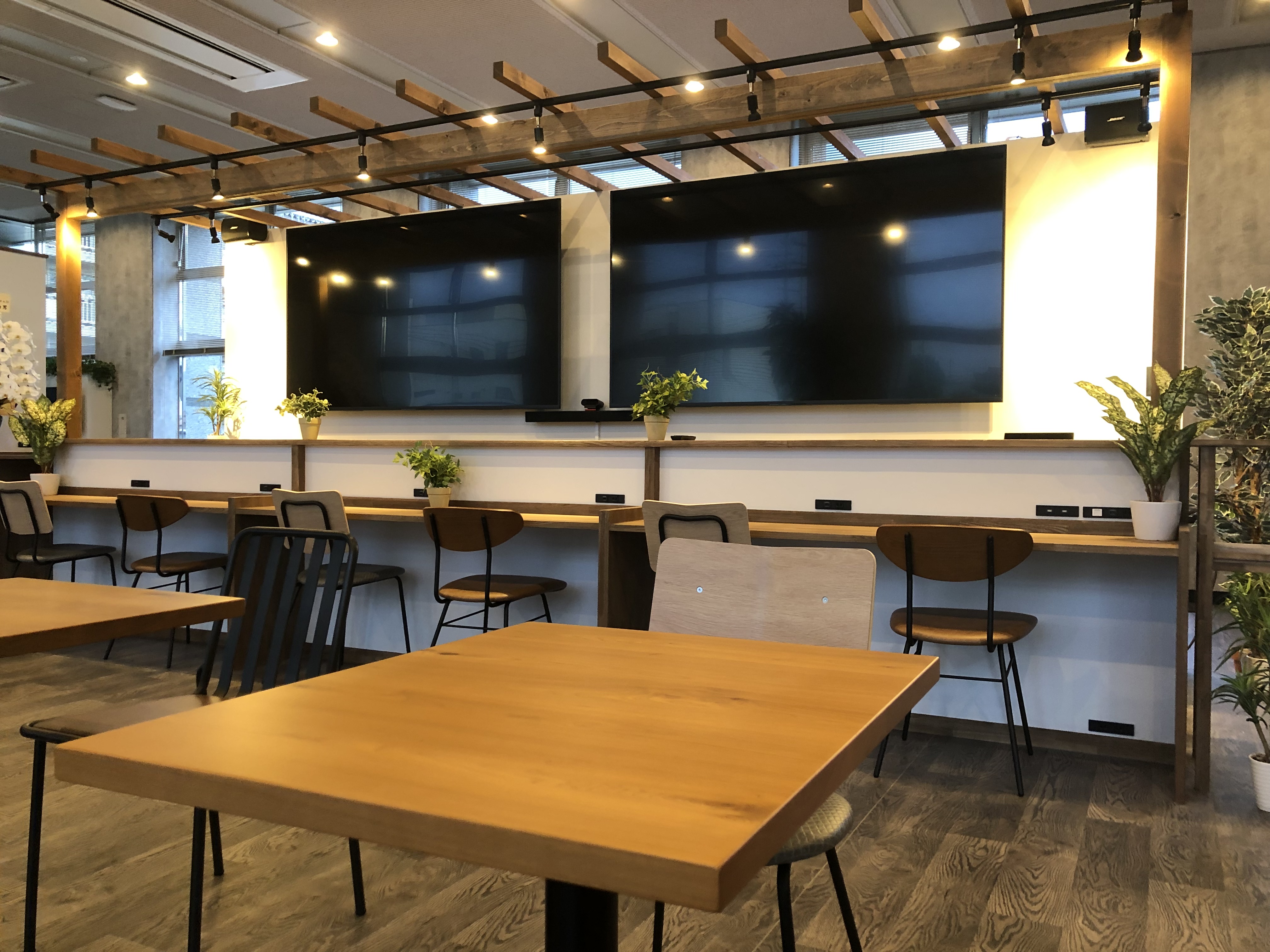 木製テーブルとカウンター席、大型モニターが並ぶ共有ワークスペース。