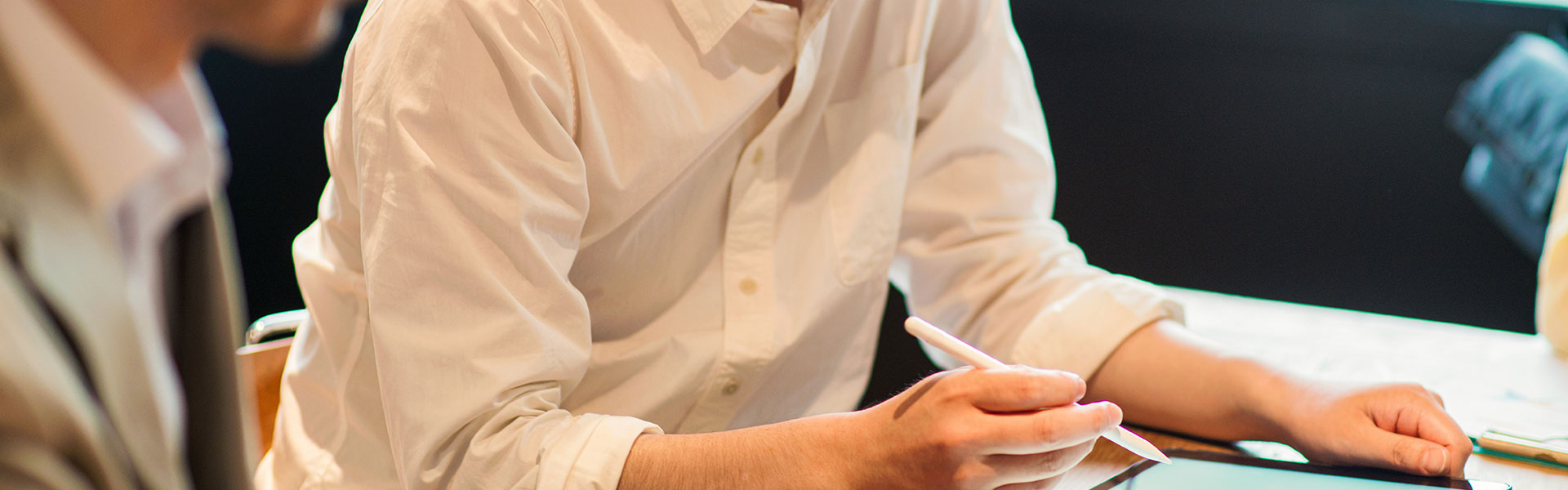 同僚と会話しながらデジタルタブレットを操作する男性