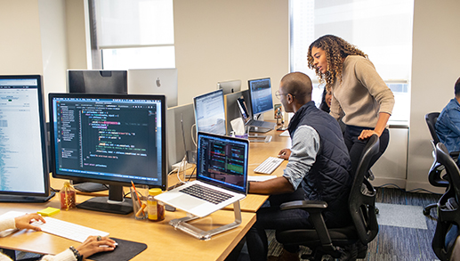 Pessoas reais, escritórios reais. Gerente de desenvolvedores colabora com desenvolvedor em espaço de trabalho empresarial.