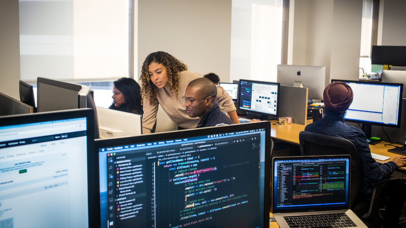 Pessoas reais, escritórios reais. Gerente de desenvolvedores colabora com colega desenvolvedor em espaço de trabalho de desenvolvedor.
