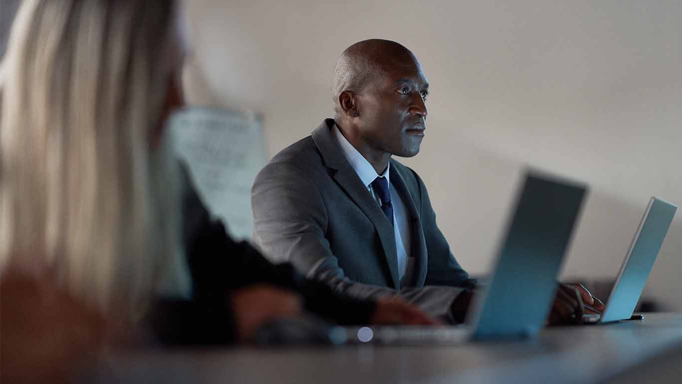 Profissionais colaborando em reunião corporativa com laptops.