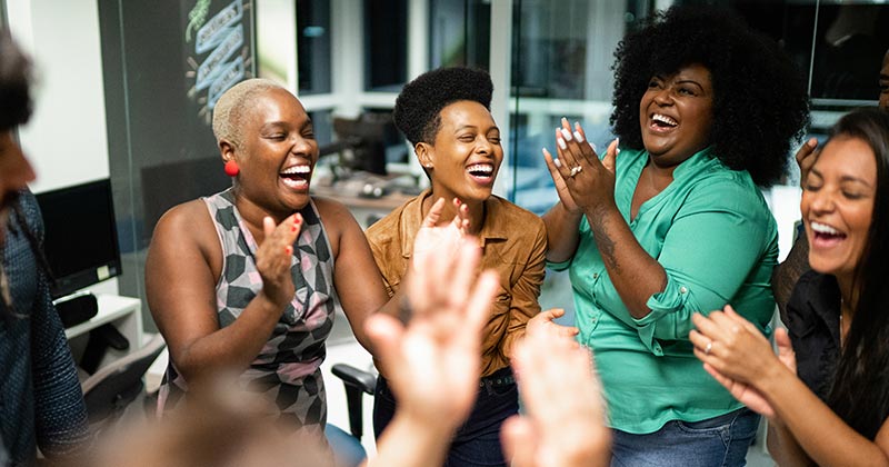 Diversas mulheres em uma roda batendo palmas e sorrindo