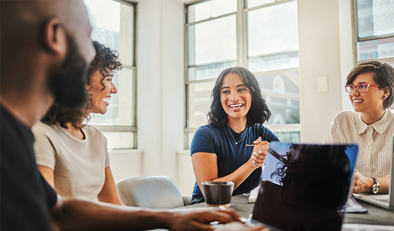 Uma pessoa usando fones de ouvido e óculos trabalha em uma mesa com um laptop em um suporte e um monitor de computador.