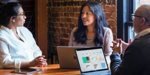 Três pessoas sentadas em frente a uma mesa com dispositivos conversando
