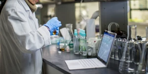 Pessoa em frente a um laboratório cheio de equipamentos médicos e um notebook