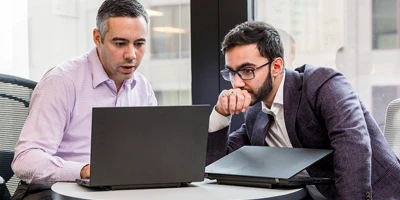 Homens em sala de reuni&atilde;o conversando e olhando para computador