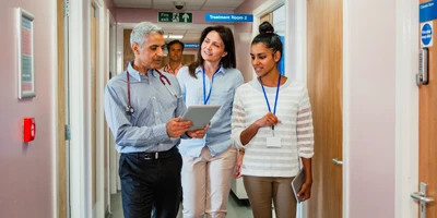 Equipe de 3 m&eacute;dicos andando pelo hospital com o tablet na m&atilde;o