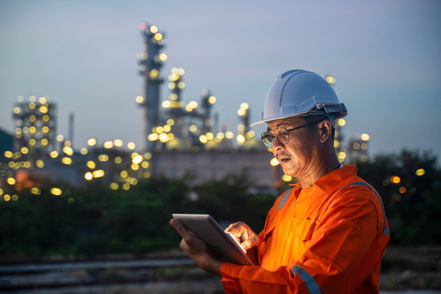 engenheiro com casco branco e uniforme naranja de seguran&ccedil;a, sustentando um tablet Surface