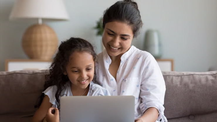 Woman and young kid sitting on a couch with a laptop on them